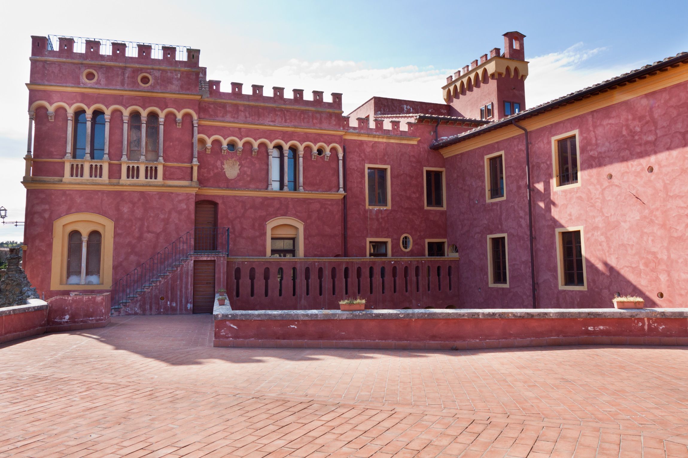 Ein historisches Gebäude mit roter Fassade, Bogenfenstern und einer zentralen Treppe.