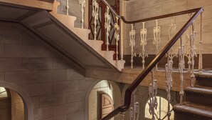Een statige trap met versierde metalen leuningen en een hanglamp.