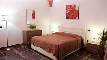 A bedroom with a bed, a nightstand, a dresser, a mirror, and a potted plant.