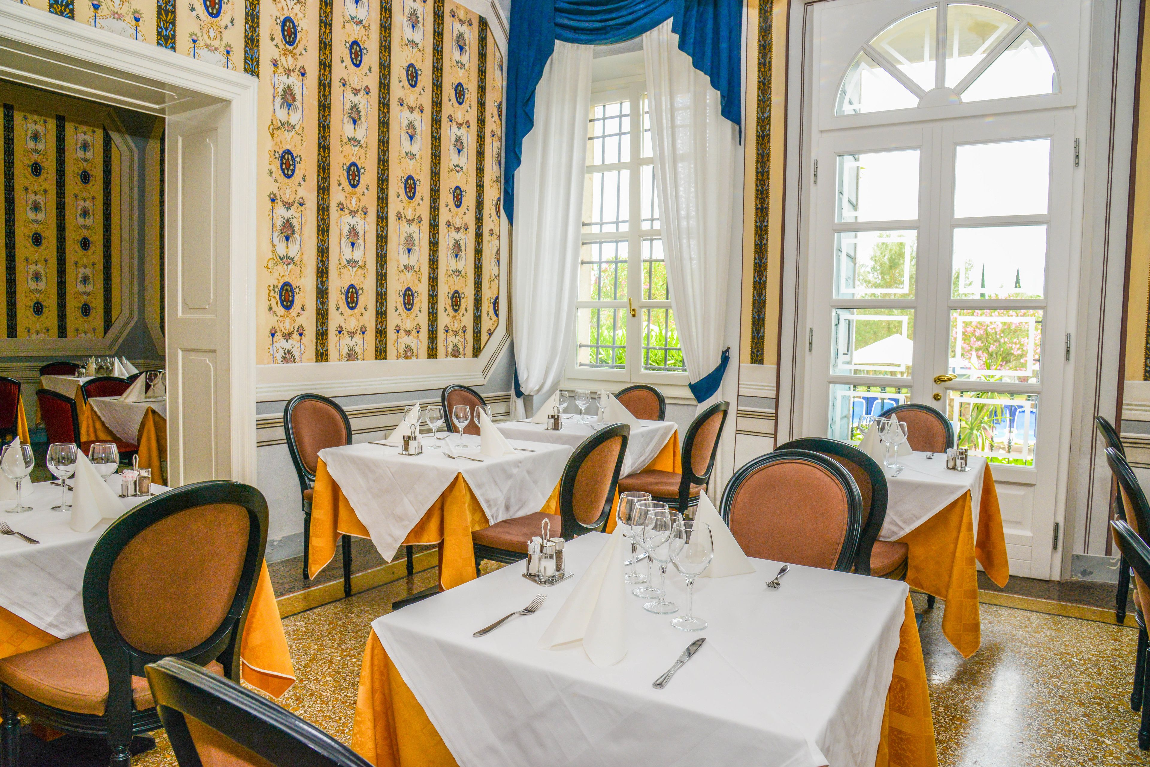 A dining area with tables set for service, chairs, and a view through a window.