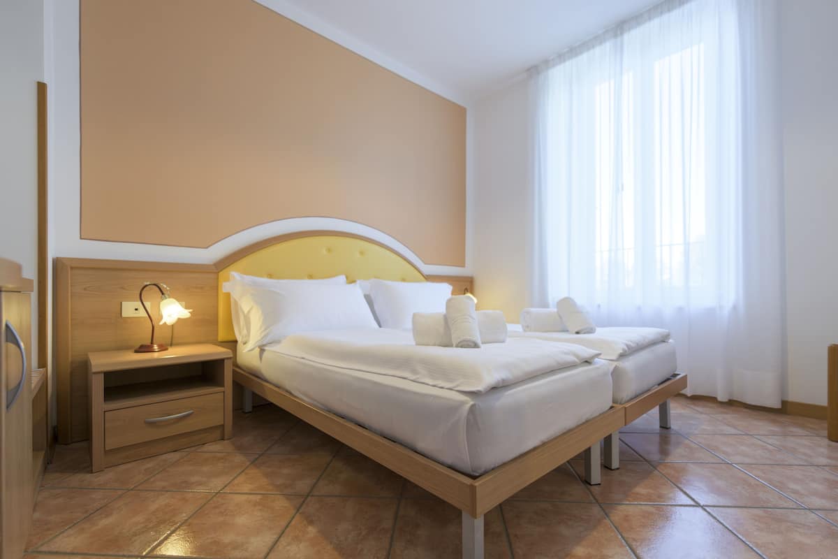 A hotel room with a bed, bedside table, and a nightstand with a lamp.