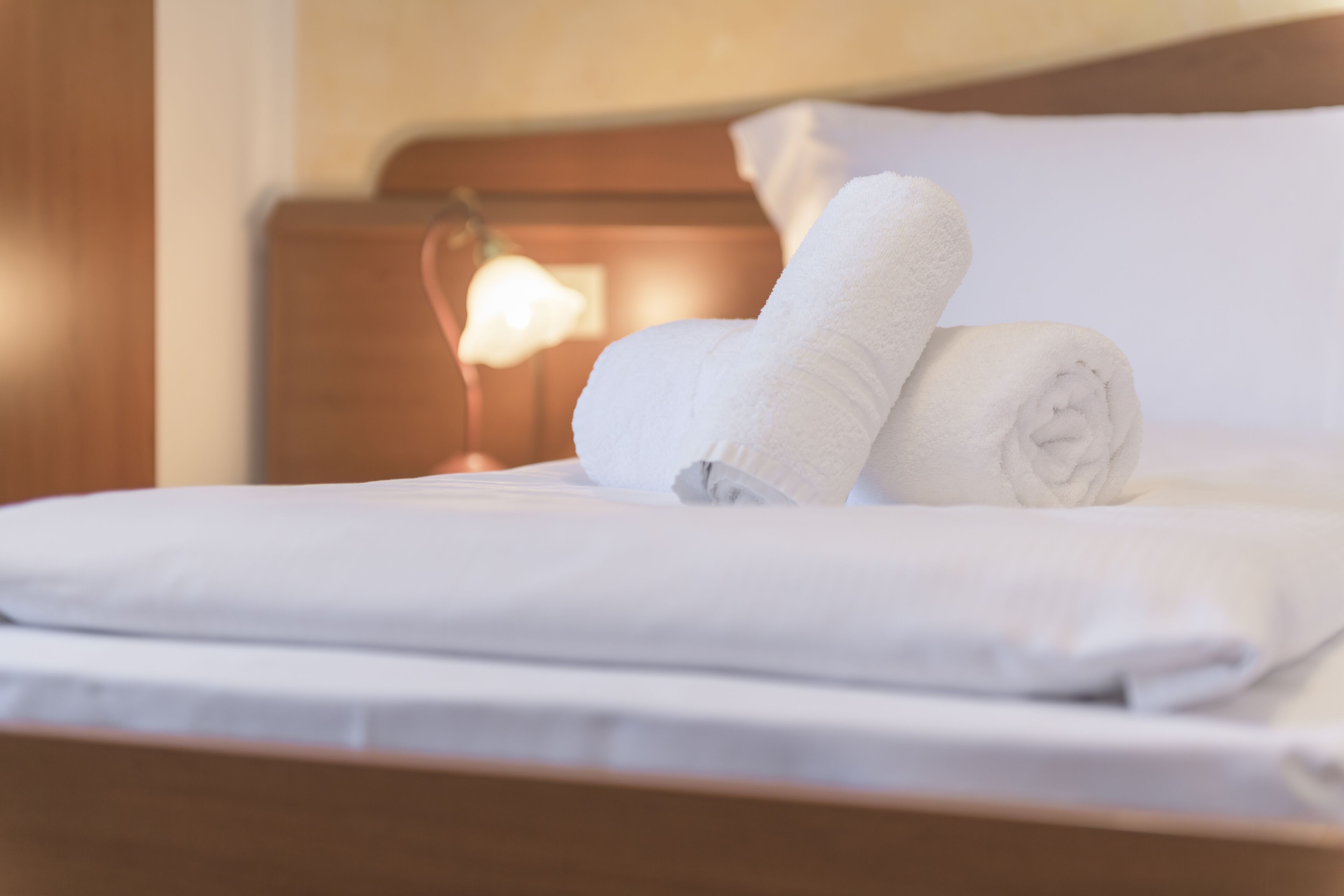 A neatly made bed with white linens and rolled towels.