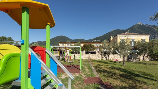 A playground with colorful equipment and a stone building in the background. - Hotel Antico Monastero (Toscolano Maderno)