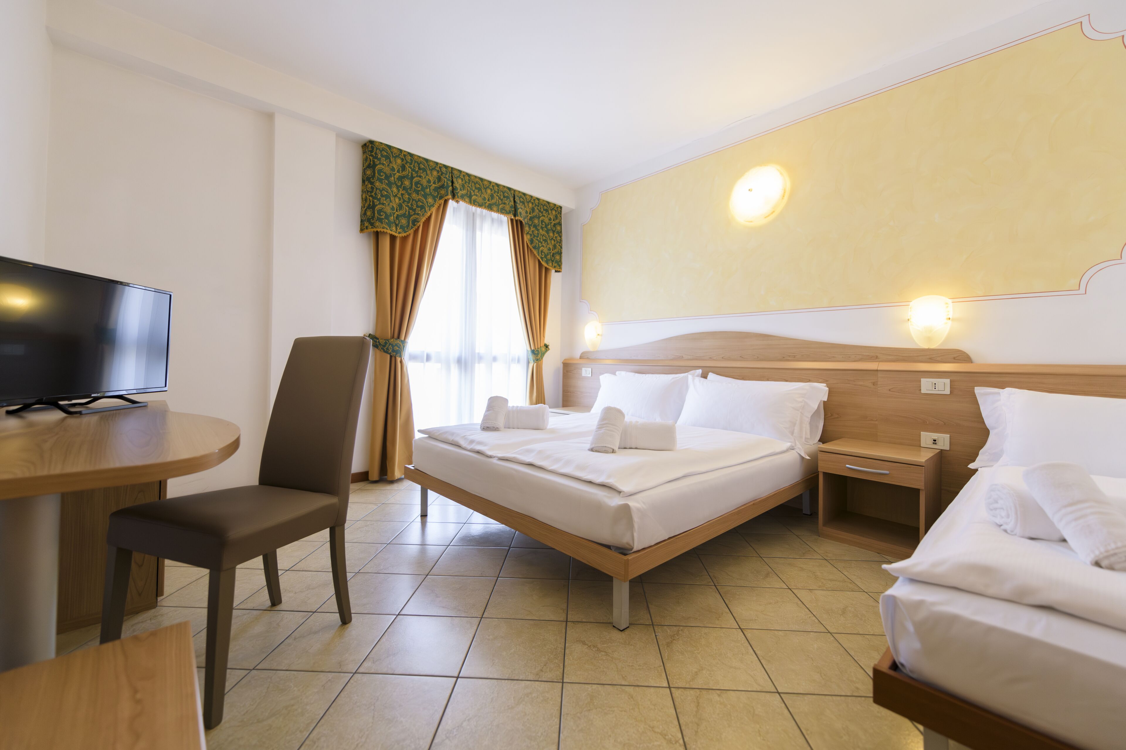 Una habitación de hotel con cama, escritorio con televisor, silla y mesita de noche.