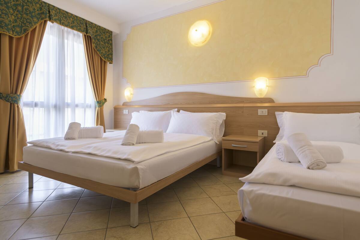 A hotel room with two beds, a wooden headboard, a nightstand, and a wall-mounted light fixture.