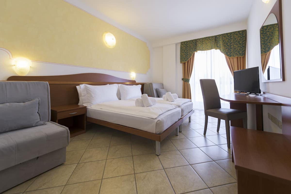 A hotel room with a bed, a desk, a chair, a sofa, and a TV.
