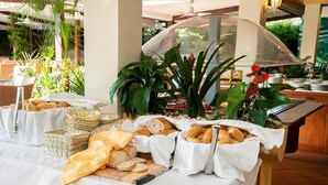 A buffet table with bread and pastries, surrounded by plants and baskets.
