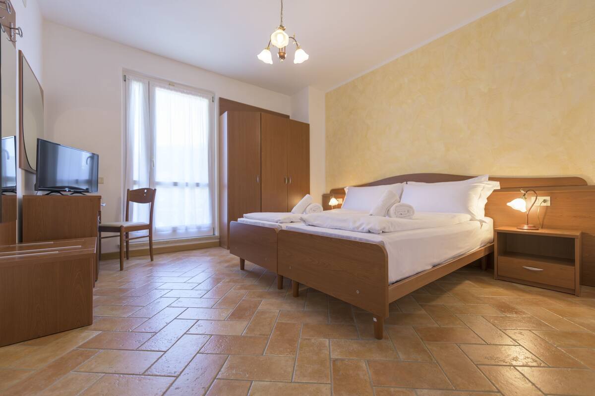 A bedroom with a bed, a TV, a chair, a wardrobe, and a nightstand.