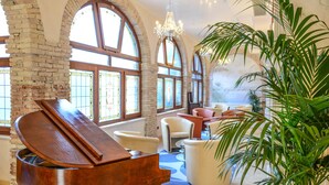 A grand piano in a spacious room with large arched windows, comfortable seating, and a chandelier.