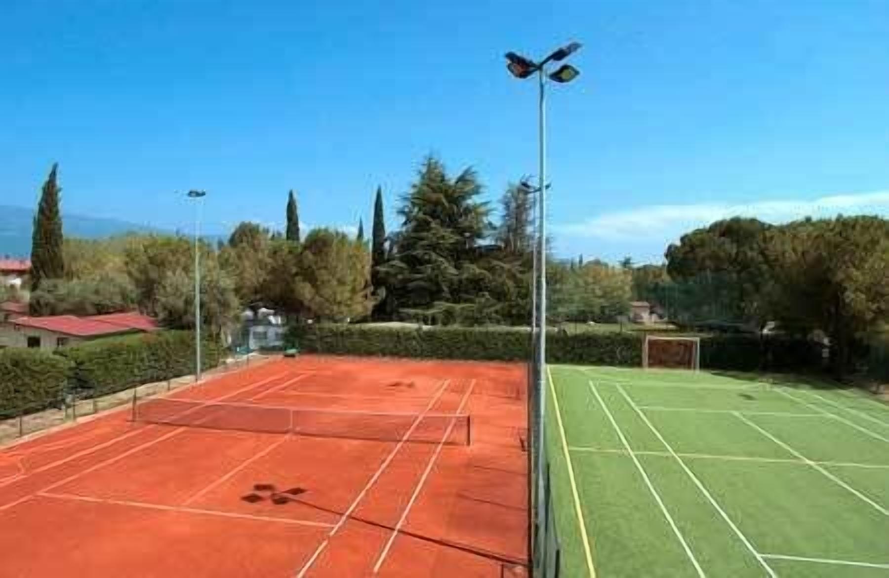 An outdoor tennis court with a net in the middle, surrounded by trees and a clear sky.