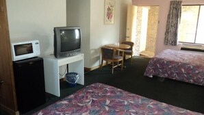 A hotel room with a television on a stand, a microwave, a small table with a chair, and two beds with floral bedspreads. - Oasis Motel (Niagara Falls)