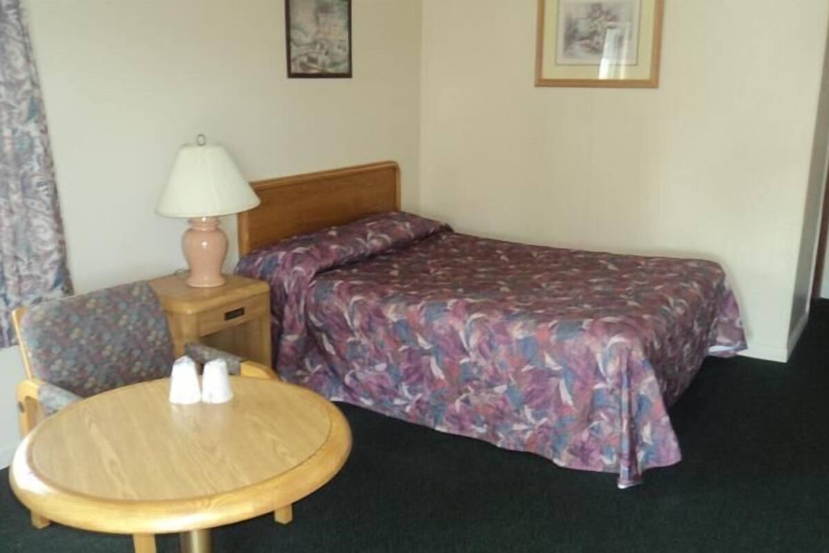 A hotel room with a bed, a chair, a small table, and a lamp.