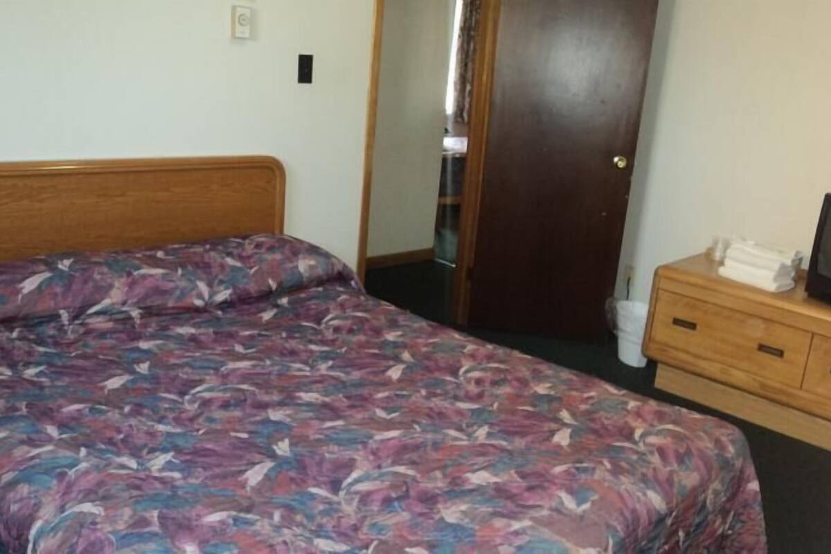 A bedroom with a bed, wooden dresser, and a television.