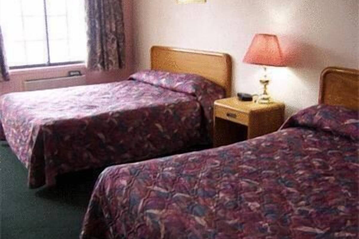 A hotel room with two single beds, a nightstand with a lamp, and a window with curtains.