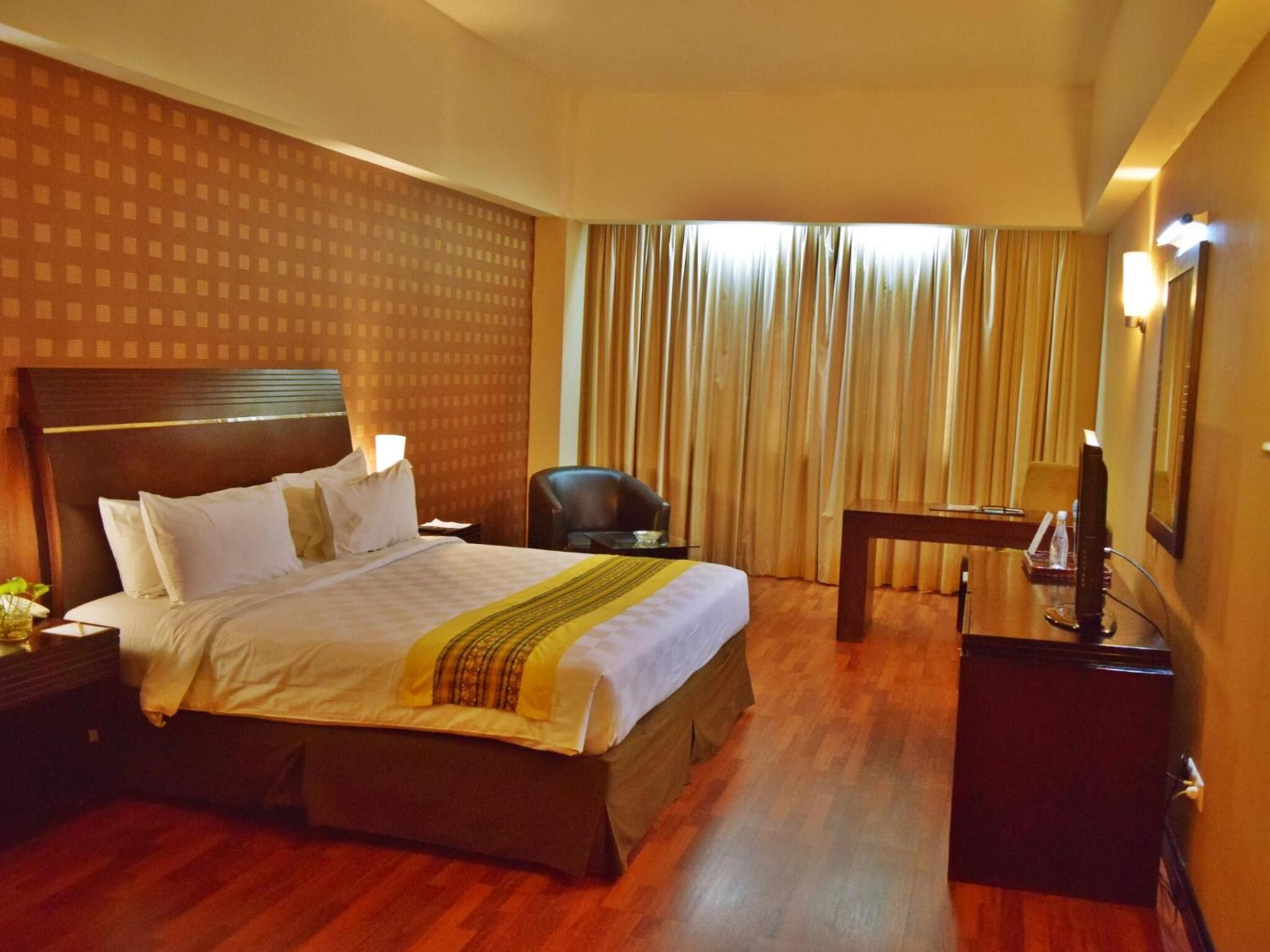 A hotel room with a large bed, a desk, a chair, a TV, and curtains.