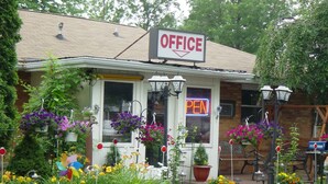 Un petit immeuble de bureaux avec une enseigne néon indiquant « OUVERT », entouré de plantes en pot et doté d’un espace de repos extérieur.