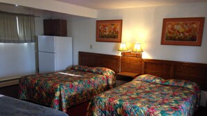 Une chambre d’hôtel avec deux lits simples, une petite table, un réfrigérateur et deux lampes fixées au mur.