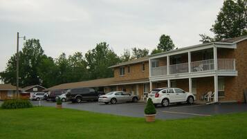 Un motel con un edificio de dos pisos, una zona de estacionamiento techada y un patio delantero con césped.