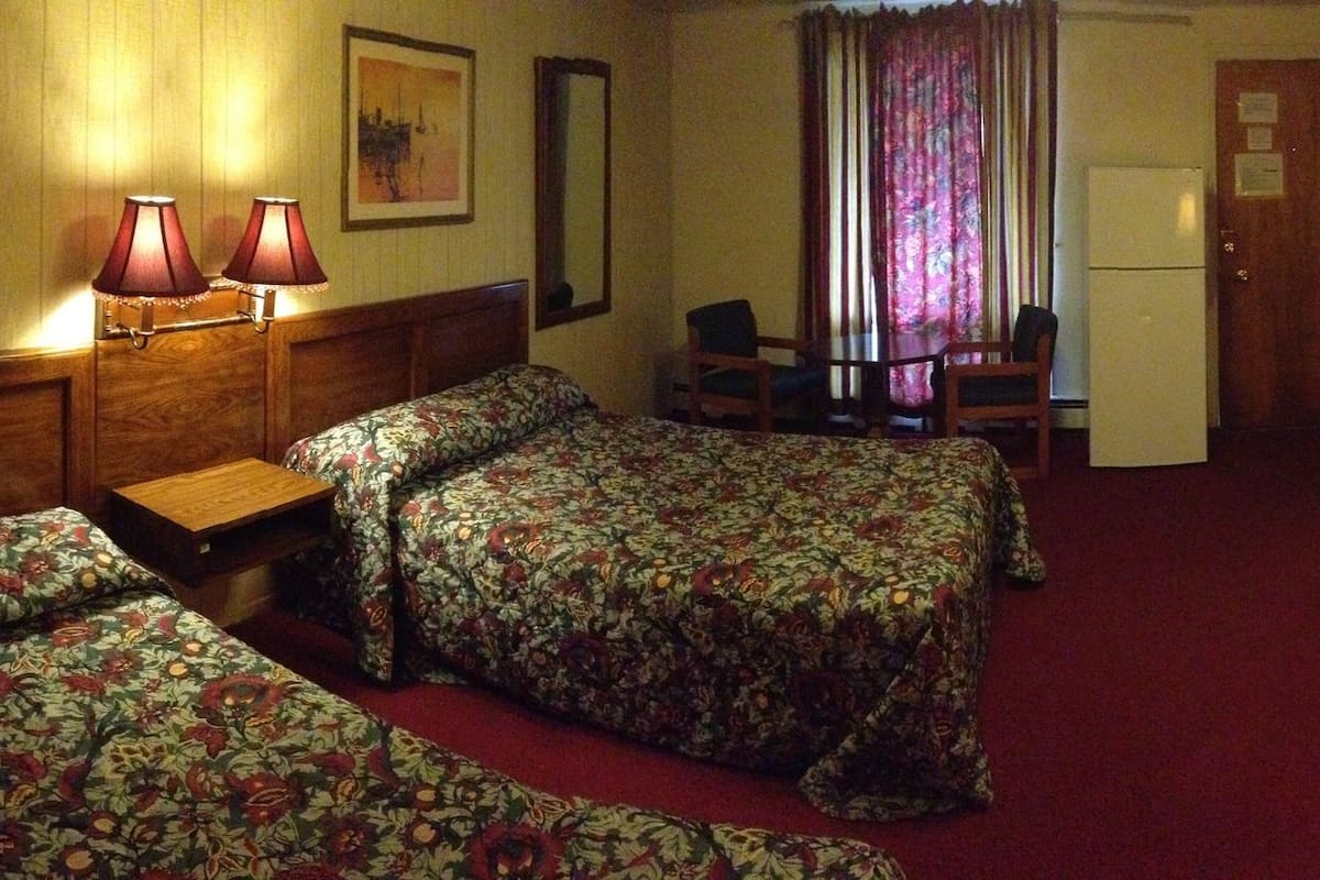 A hotel room with two beds, a desk, a lamp, a microwave, and a TV.
