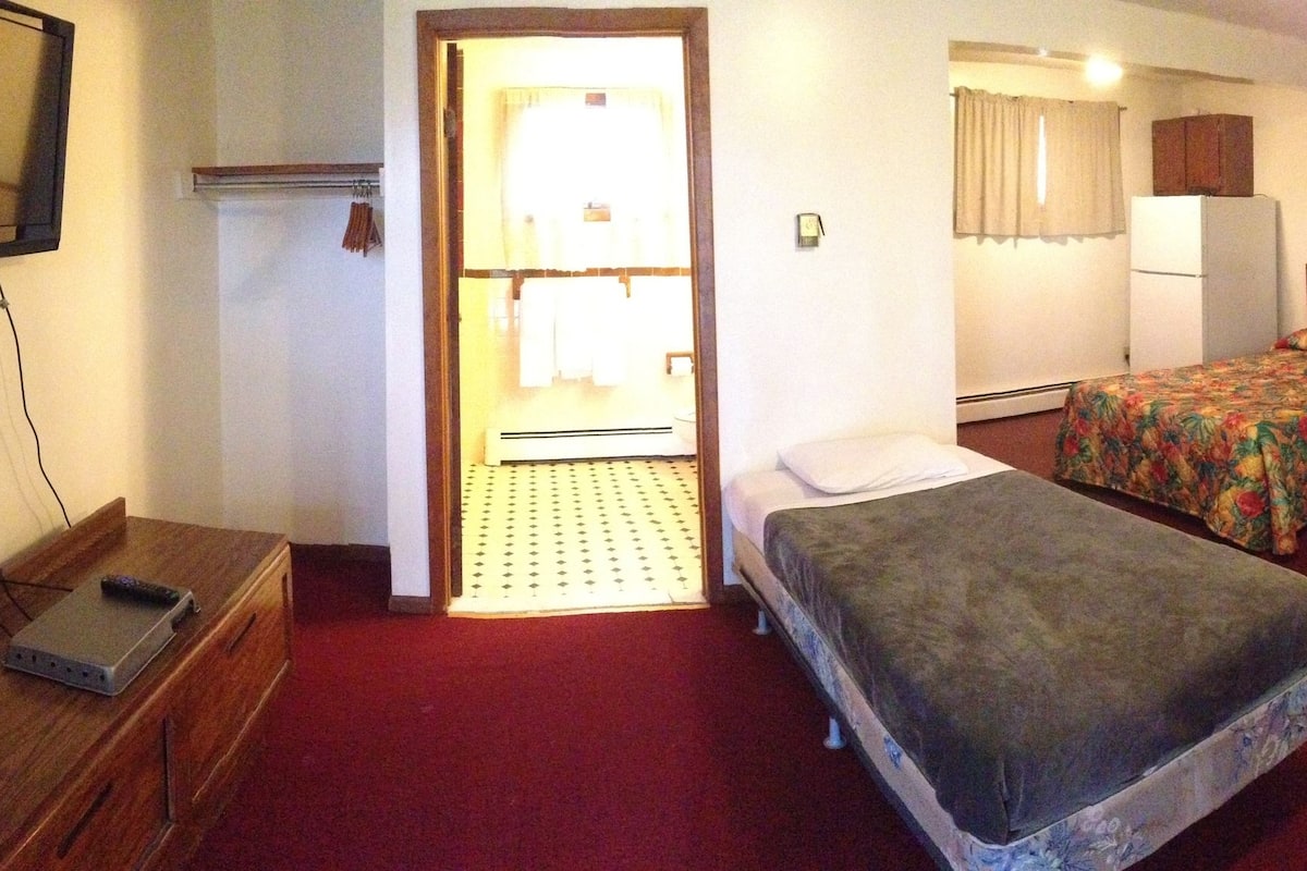 A room with two single beds, a desk, a chair, a television, and a refrigerator.