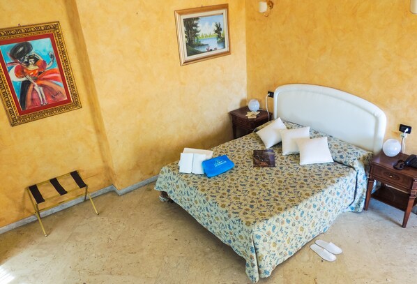 Una habitación de hotel con cama, mesita de noche, lámpara, cuadro enmarcado y un taburete pequeño.