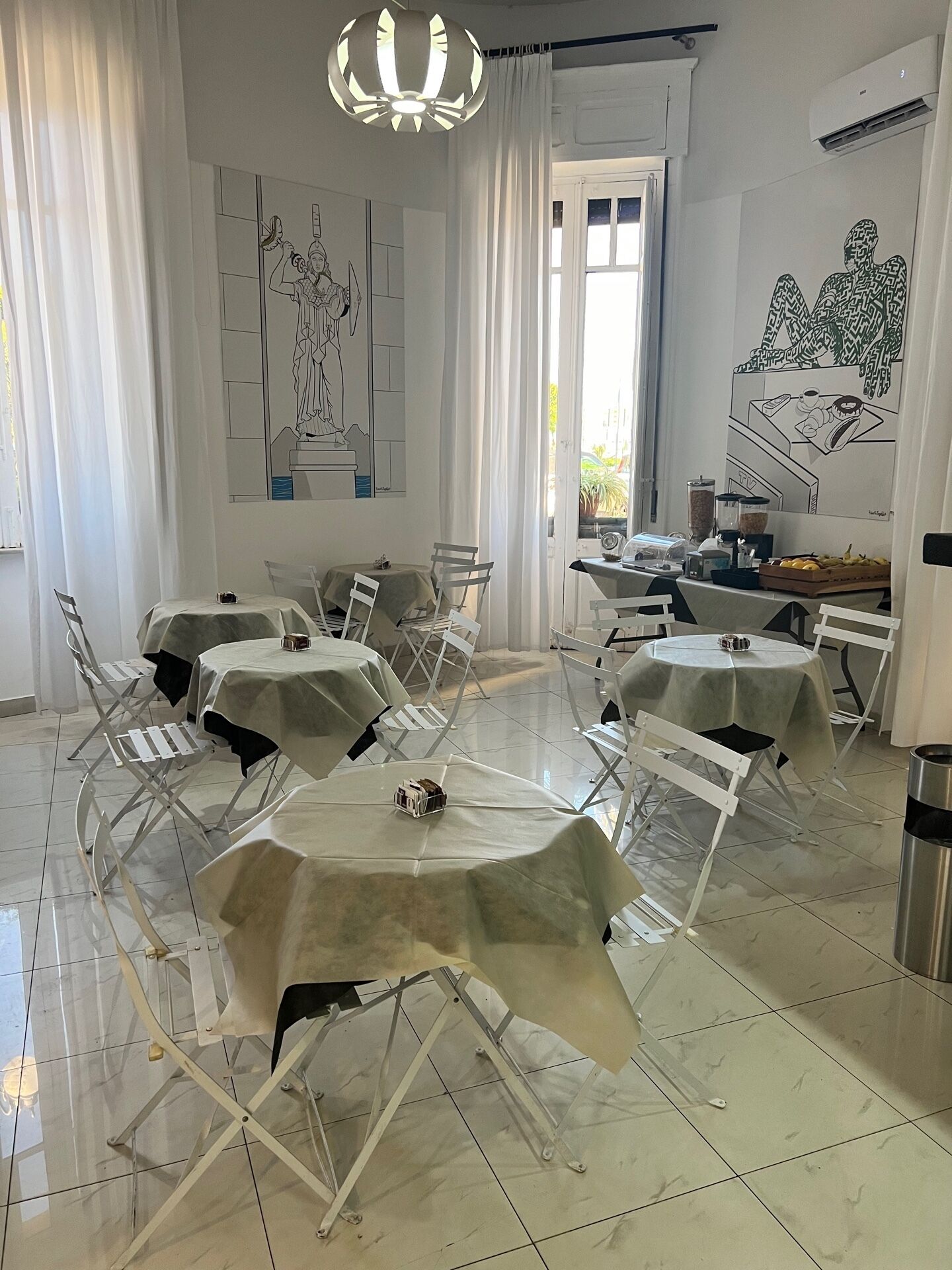 A dining area with white tables and chairs, a chandelier, and artwork on the walls.