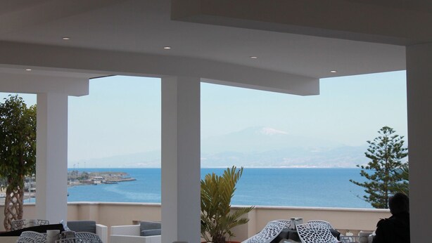 A terrace with white columns, outdoor seating, and a view of the sea and distant mountains. - Lungomare Hotel (Reggio Calabria)