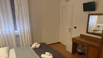 A hotel room with a bed, a small desk, a mirror, a television, and a window with curtains.