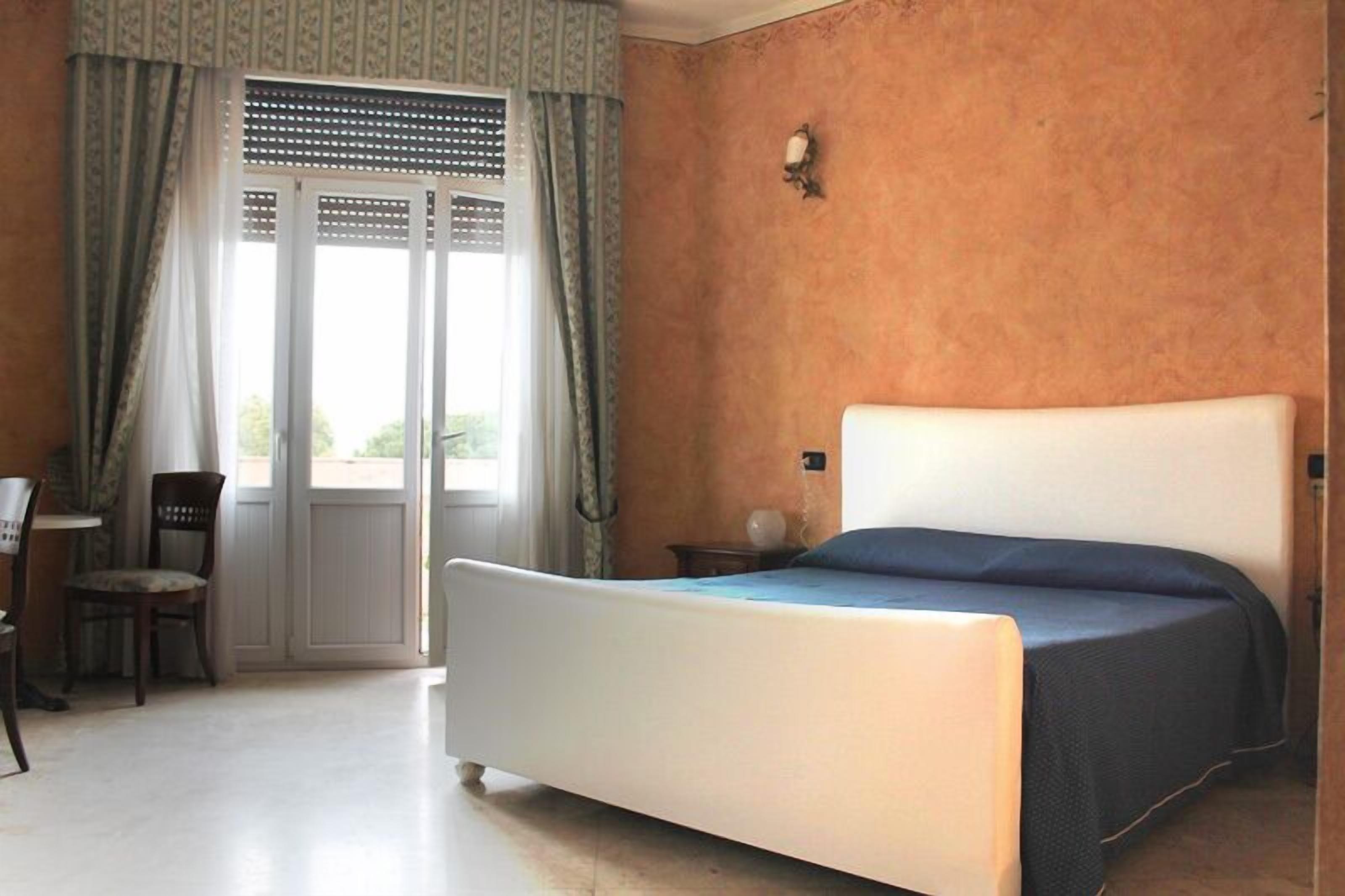 Une chambre à coucher avec un lit, une chaise, une table et une fenêtre avec des rideaux.