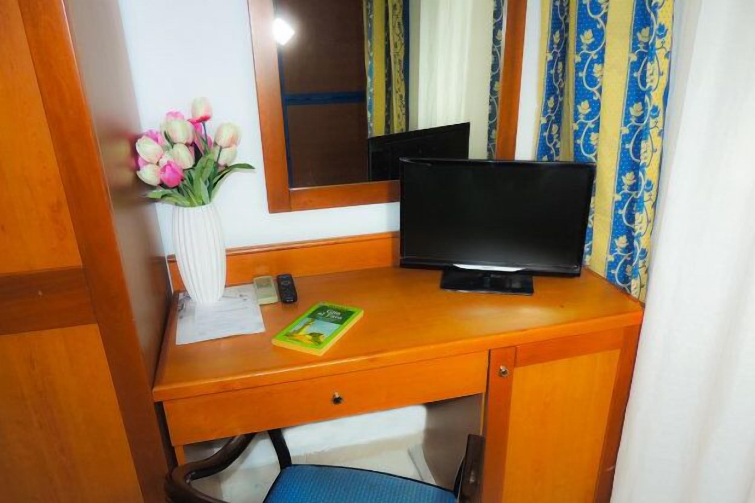 A wooden desk with a television, a vase of flowers, and a book.