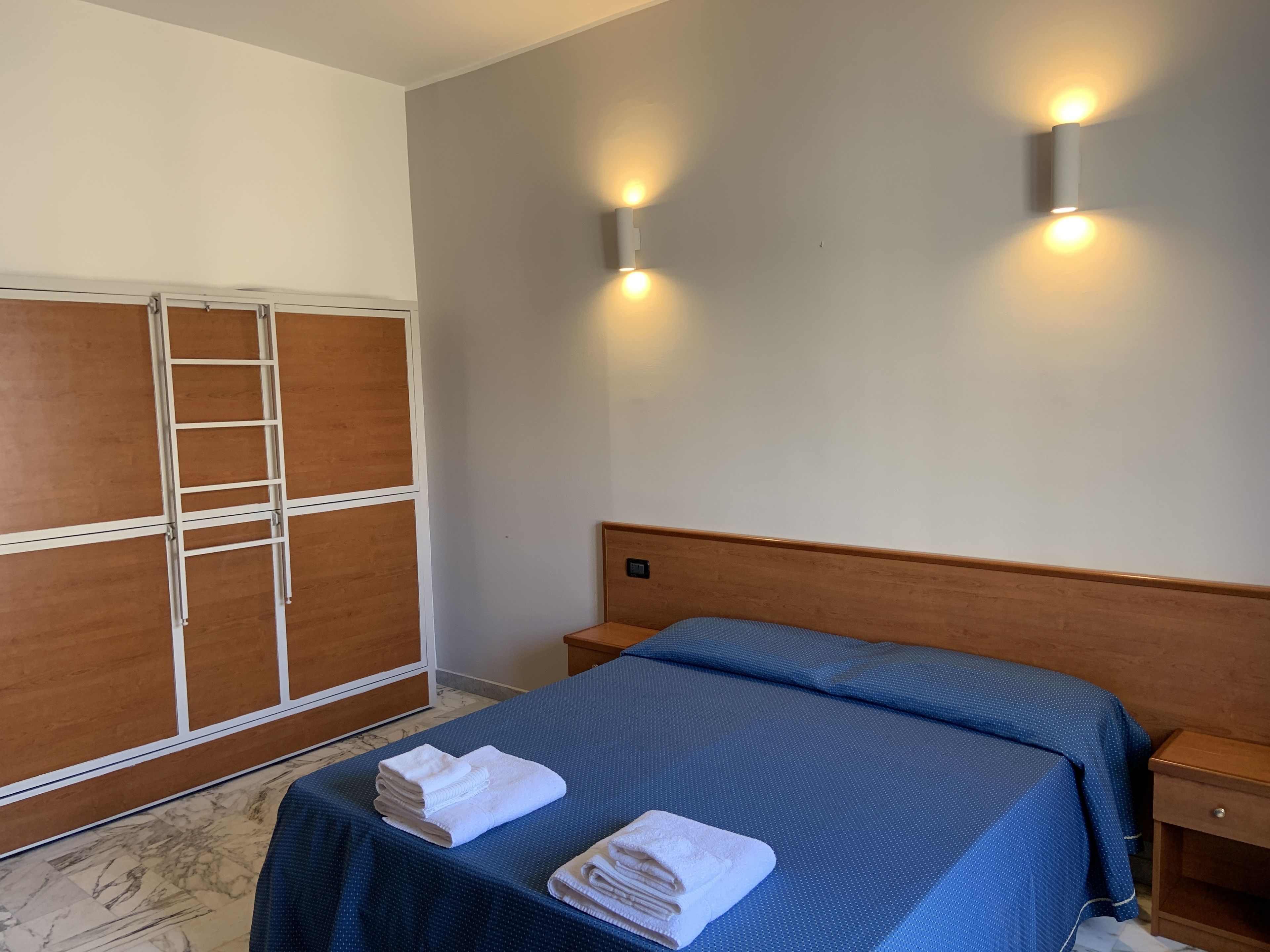 Een hotelkamer met een bed, een houten garderobe en twee wandlampen.