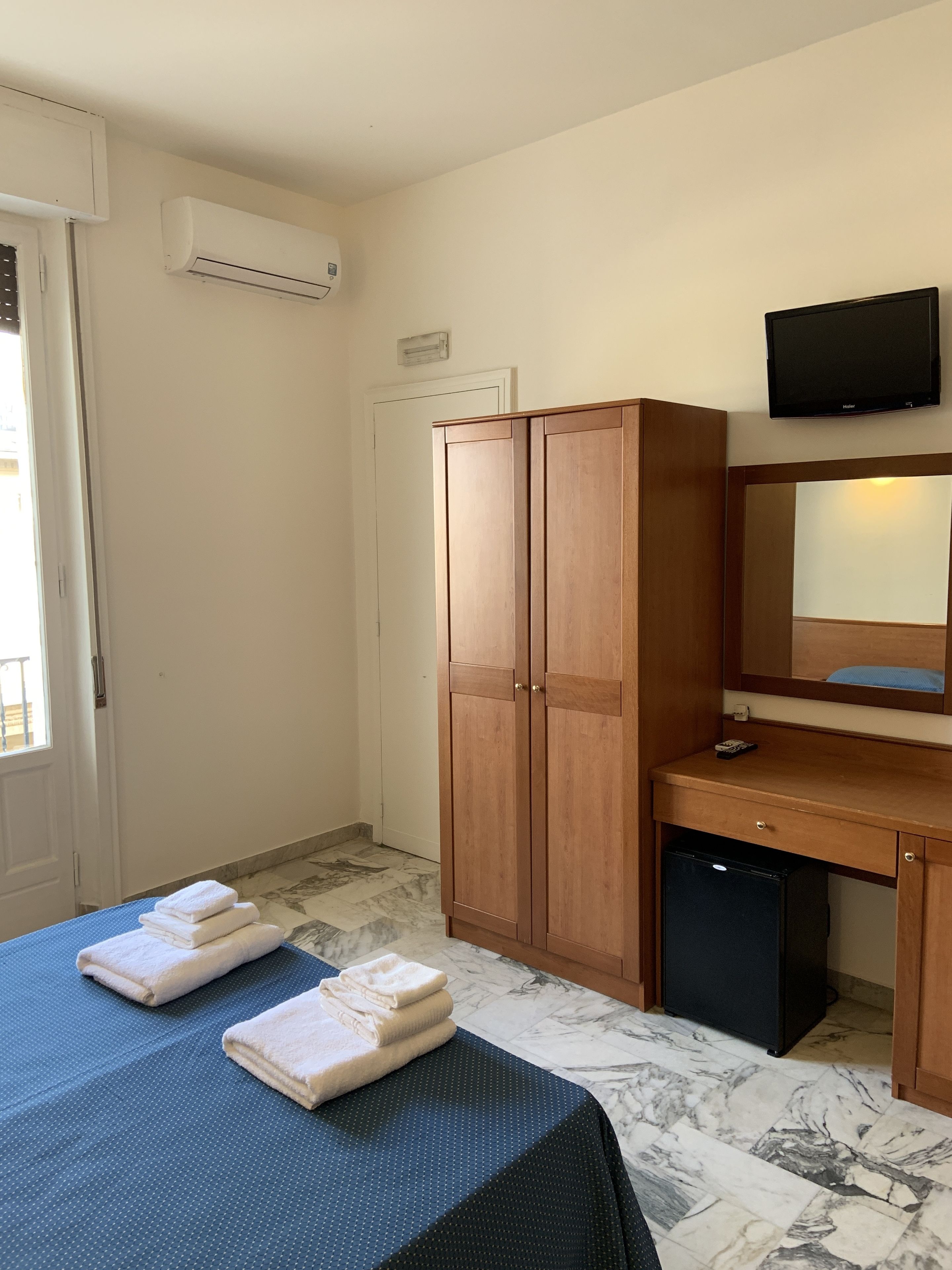 Una habitación de hotel con una cama, un armario de madera, un escritorio con televisor y un refrigerador pequeño.
