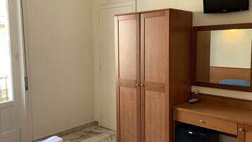 Una habitación de hotel con una cama, un armario de madera, un escritorio con televisor y un refrigerador pequeño.