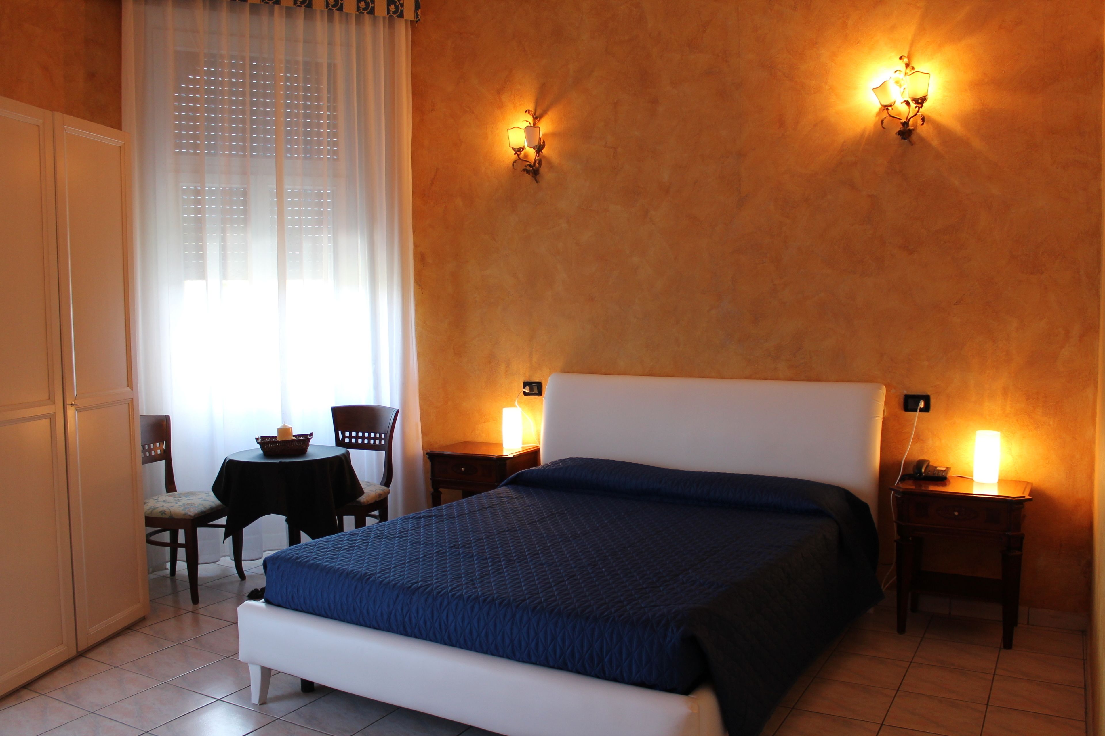Habitació d'hotel amb un llit, dues taules de nit, una cadira, una taula petita i una finestra amb cortines.