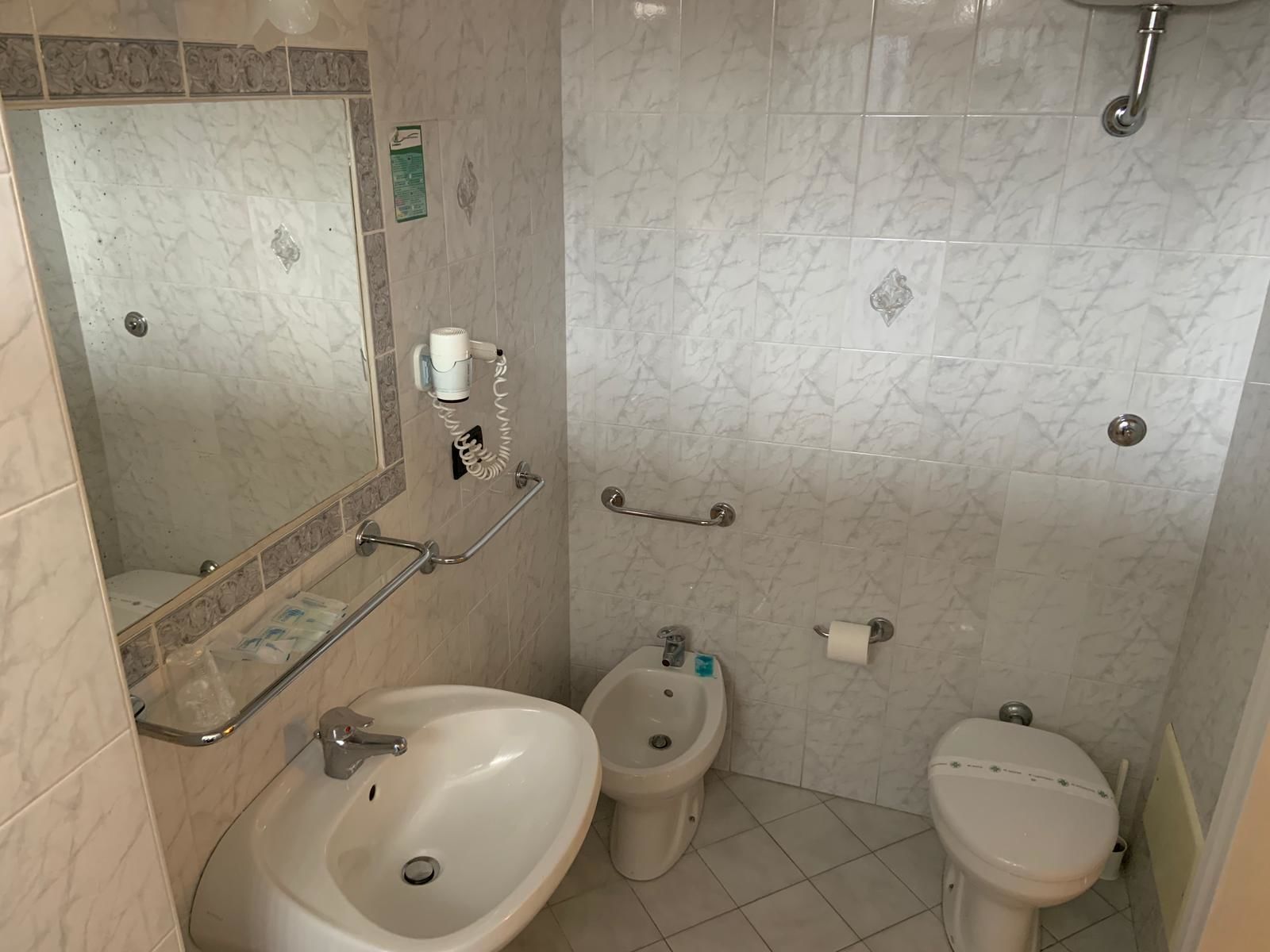 Baño con lavamanos, bidé, inodoro y un secador de pelo fijado en la pared.