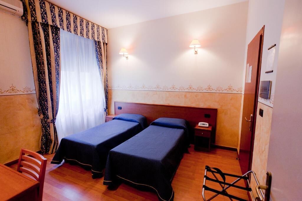 Ein Hotelzimmer mit zwei Einzelbetten, einem Holztisch, einem Stuhl, einer Schreibtischlampe und einem Telefon.