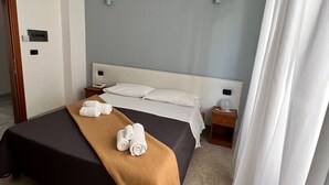 A hotel room with a bed, a bedside table, a nightstand, and a door. - Lungomare Hotel (Reggio Calabria)