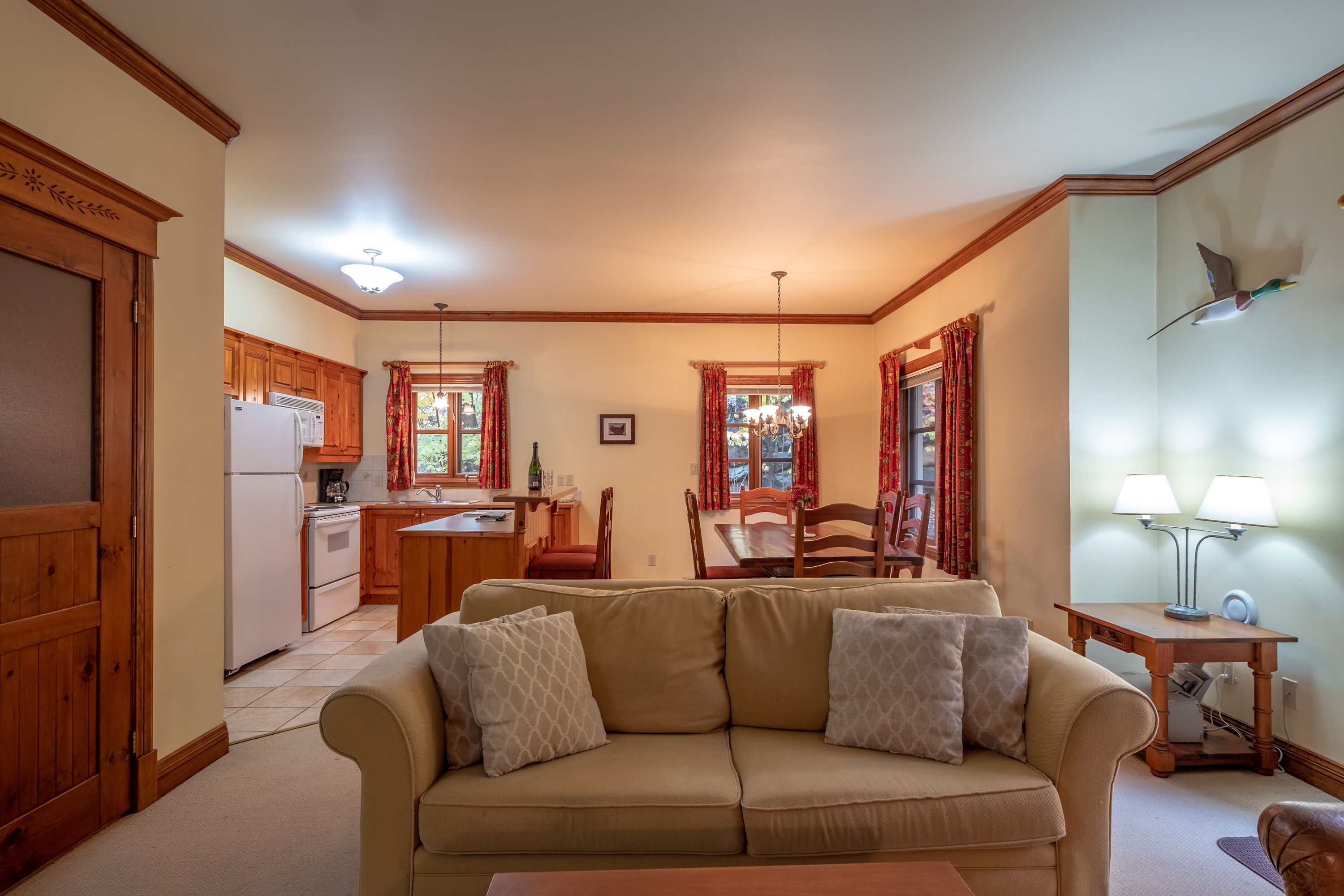 Una sala de estar acogedora con un sofá color beige, armarios de madera y un comedor con cortinas rojas.