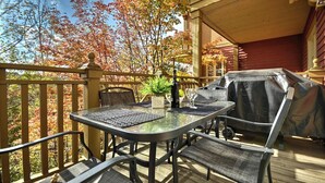 An outdoor patio with a table and chairs, a grill, and a view of autumn trees. - Le Plateau – RVMT (Mont-Tremblant)