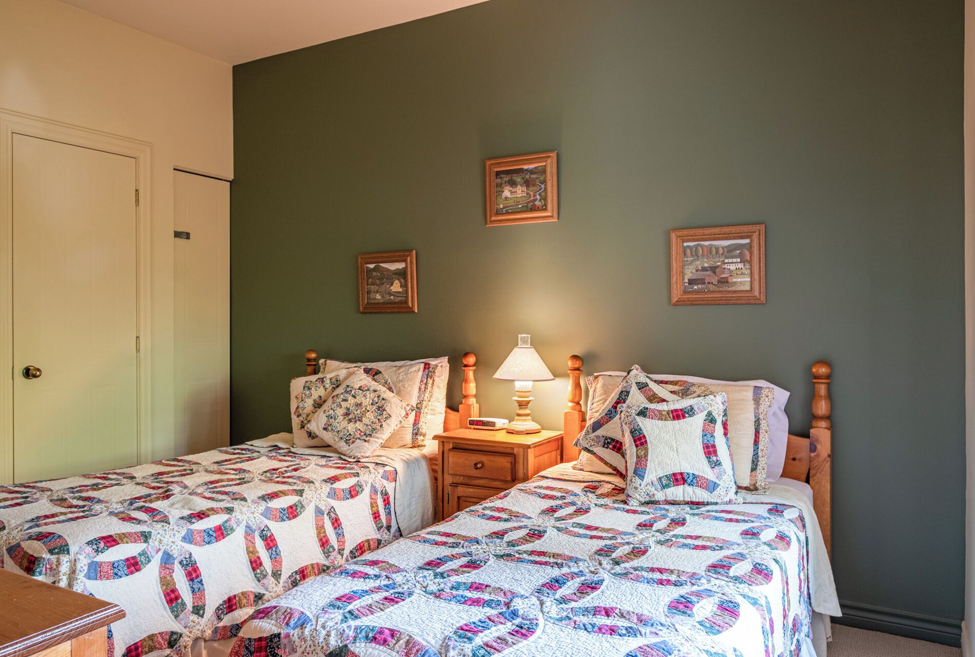 A bedroom with two single beds, a nightstand with a lamp, and three framed pictures on the wall.