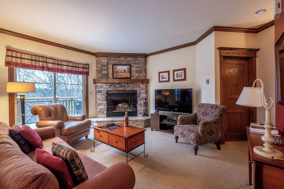 Una sala de estar acogedora con chimenea de piedra, sillones de cuero, un sofá y un televisor.