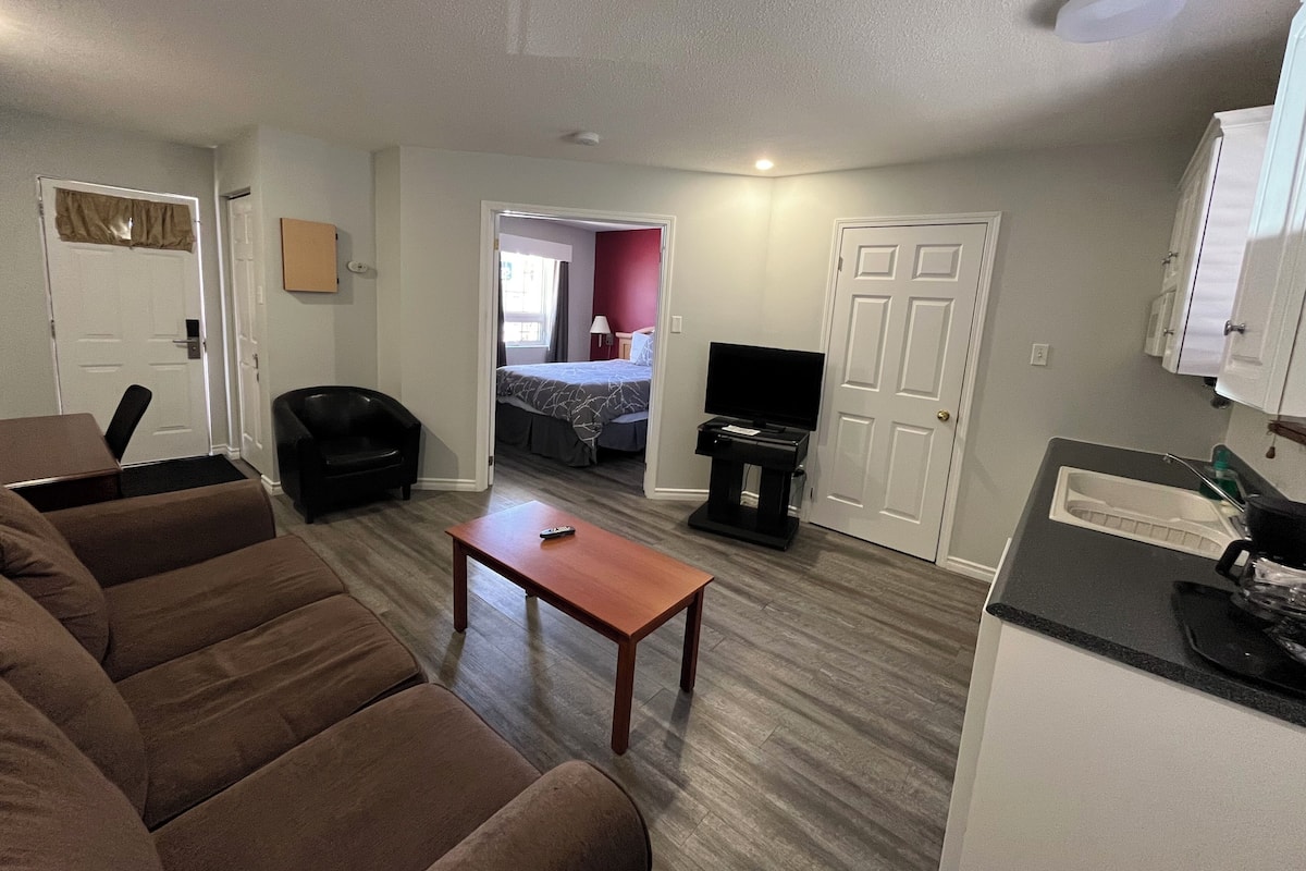 A compact hotel room with a living area, a kitchenette, a bed, and a bathroom.