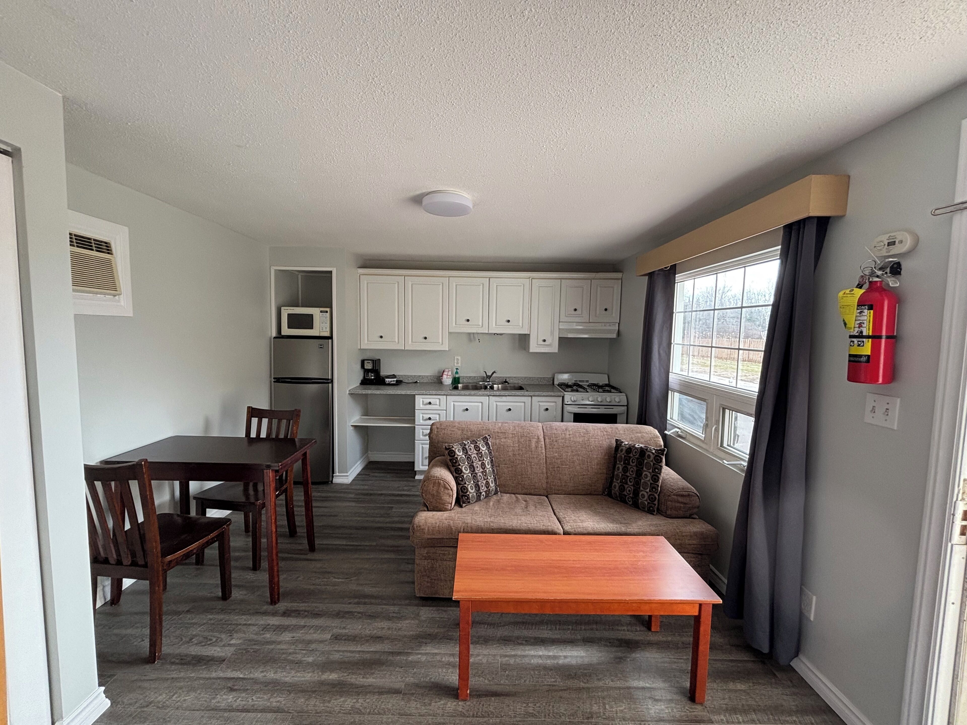 Een ruimtelijke woonruimte met een kitchenette, een eethoek en een zithoek met een bank en tafel.