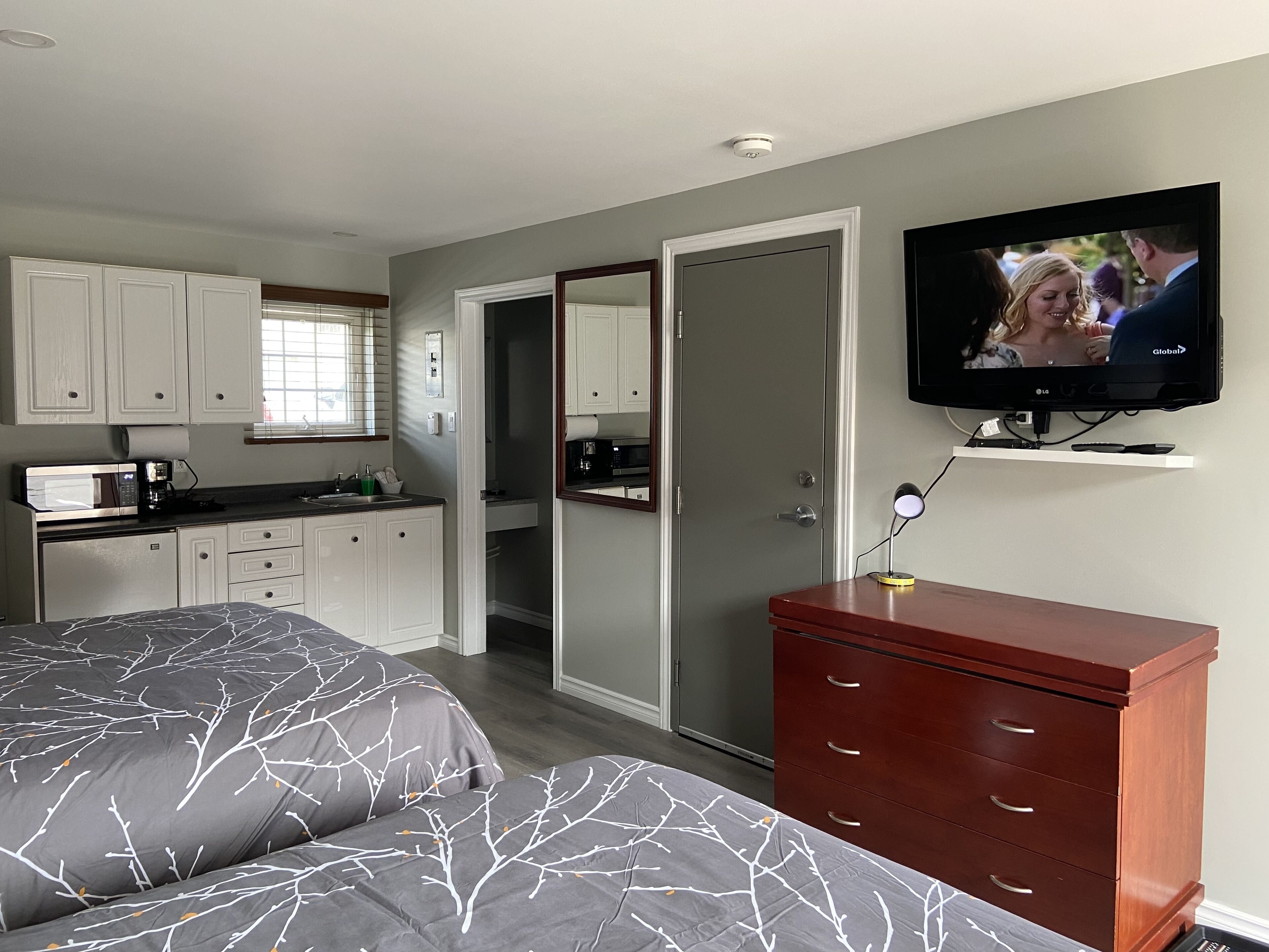 A bedroom with two beds, a TV, a dresser, and a kitchenette.