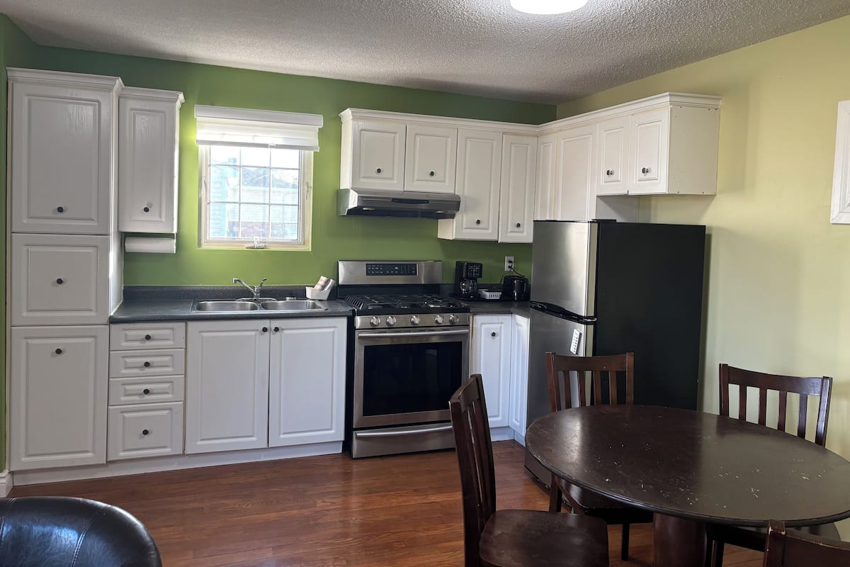 A kitchen with white cabinets, a stainless steel refrigerator, a stove, and a dining table with chairs.