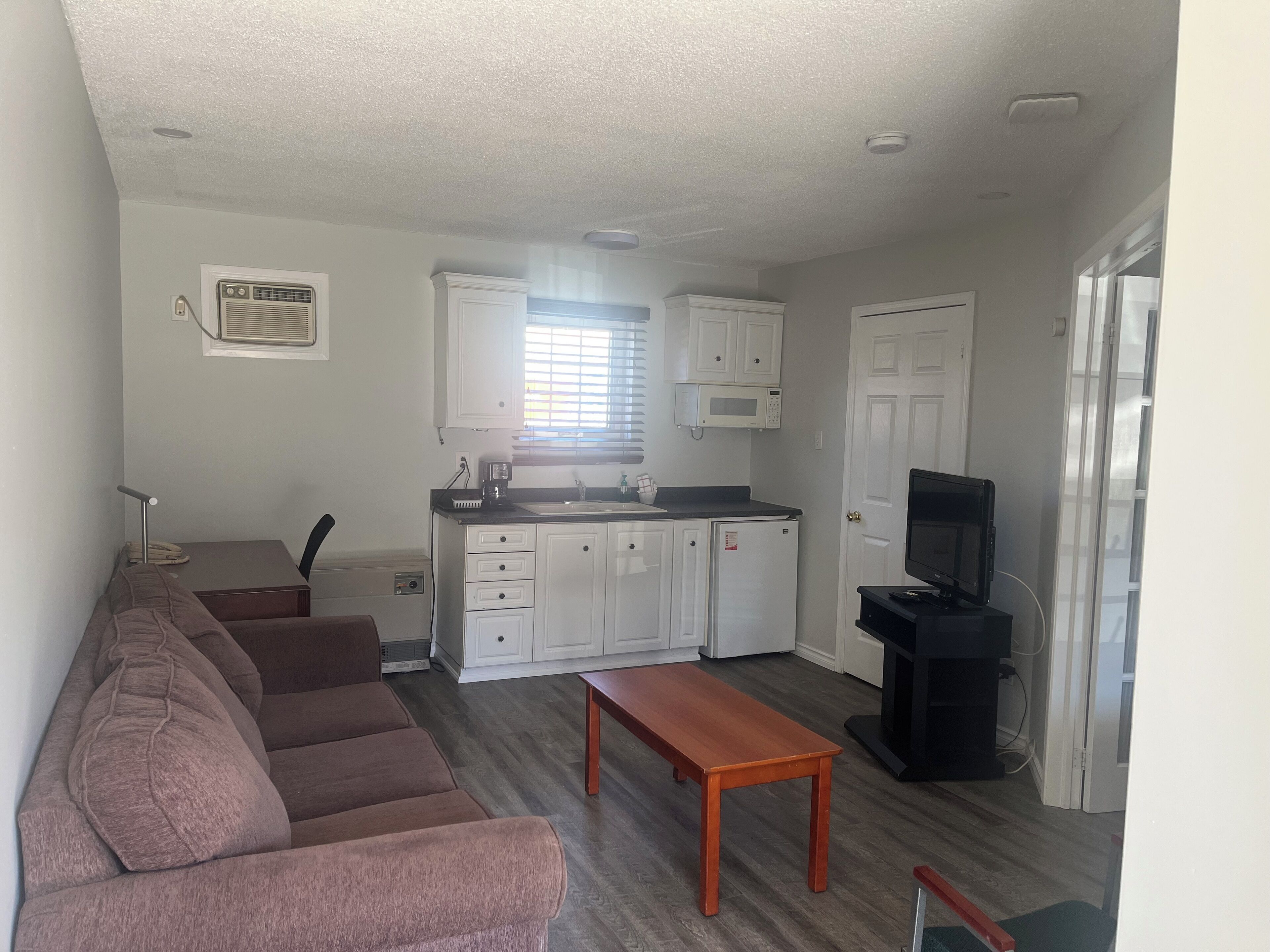 Un espacio habitable compacto con kitchenette, un sofá, una mesa de madera y un televisor.