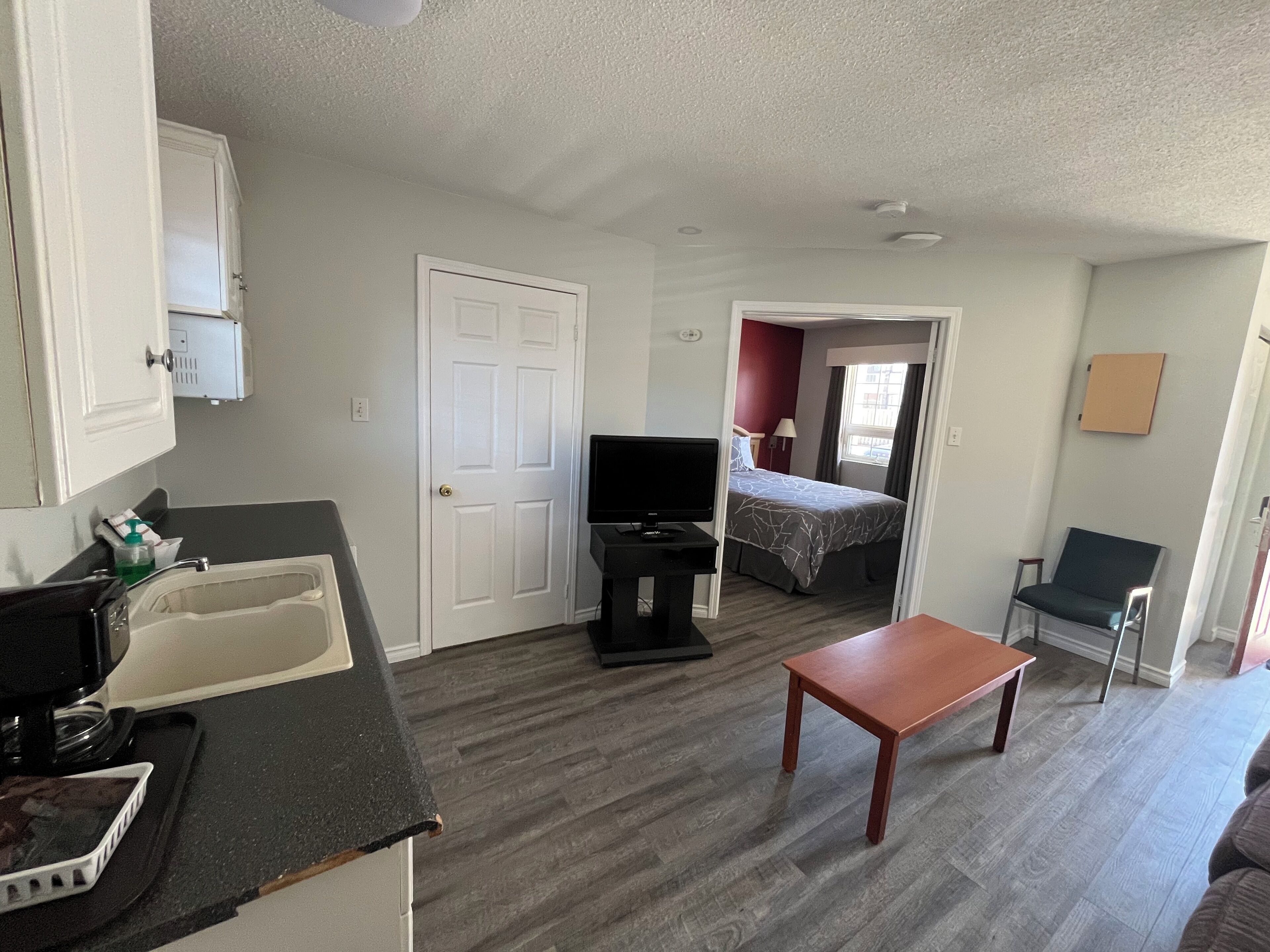 A compact hotel room with a kitchenette, a television, a bed, and a seating area.