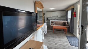 Um espaço compacto com televisão, mesa de madeira, sofá, cozinha e espelho.