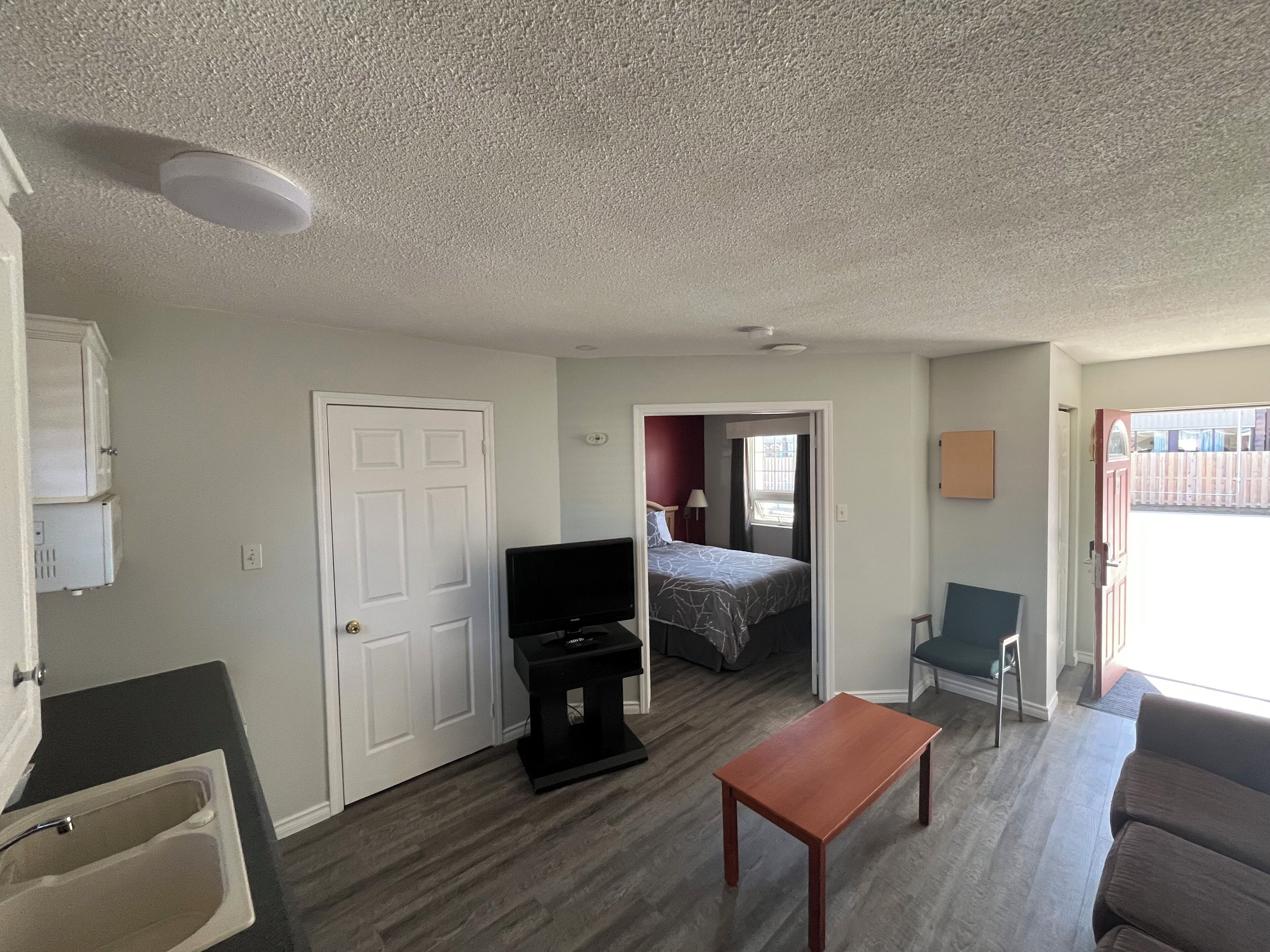 Una habitación pequeña con cama, televisión, una mesita y una silla.