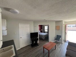 Una habitación pequeña con cama, televisión, una mesita y una silla.